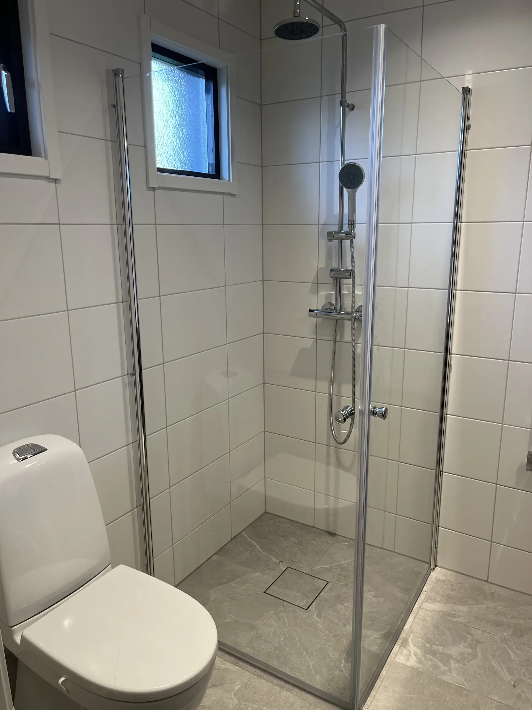 Duschhörna med glasvägg och kuvertskärning i klinkergolvet för korrekt fall mot golvbrunnen