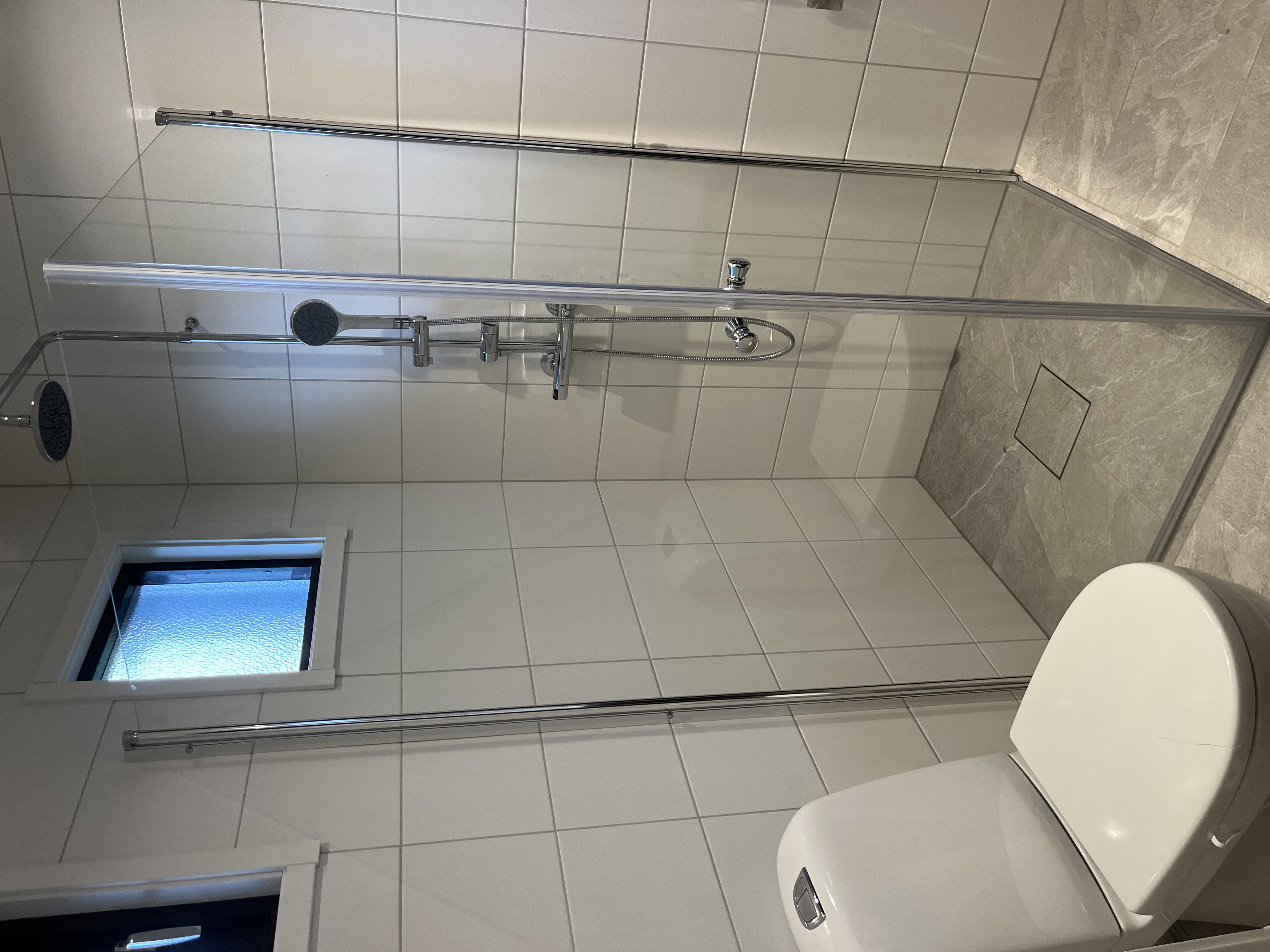 Duschhörna med glasvägg och kuvertskärning i klinkergolvet för korrekt fall mot golvbrunnen