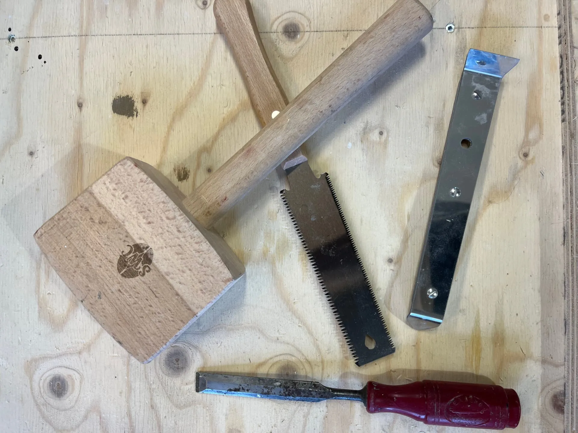 Träklubba, japansåg, stämjärn och stålskrapa på en arbetsbänk av plywood