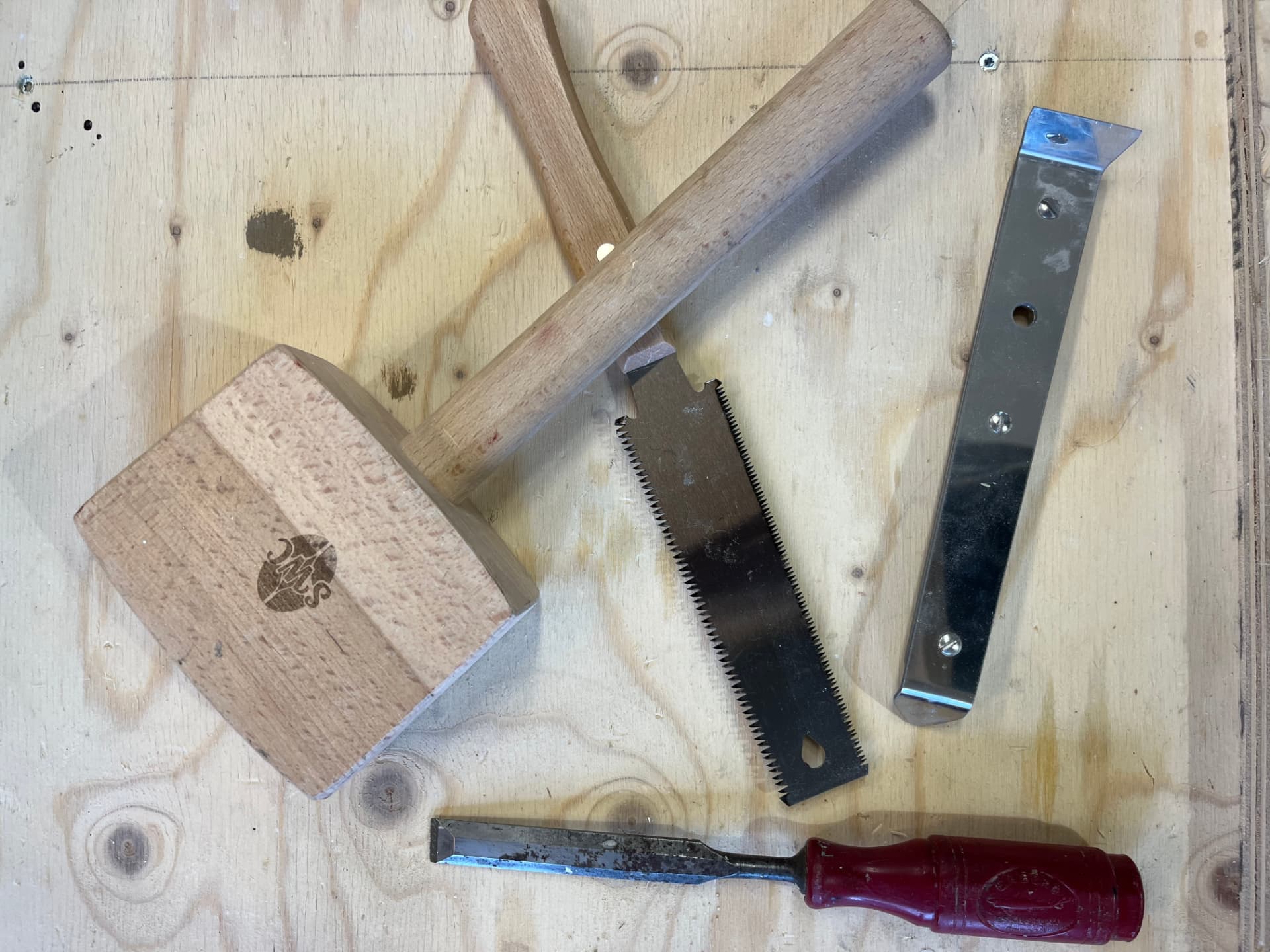 Träklubba, japansåg, stämjärn och stålskrapa på en arbetsbänk av plywood
